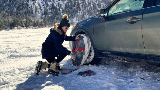 A person mounting snow socks on front wheels of a car in winter landscape