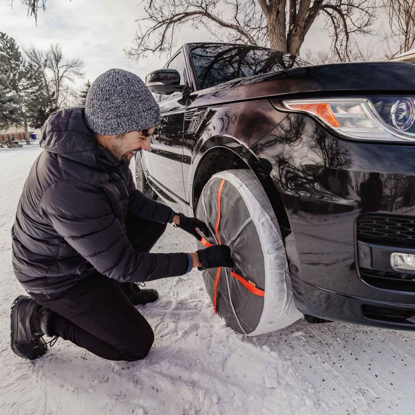Man installs snow socks on Land Rover SUV on snow