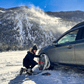 AutoSock snow chains being mounted by a woman on front wheels of a passenger car, standing on snow in mountain region